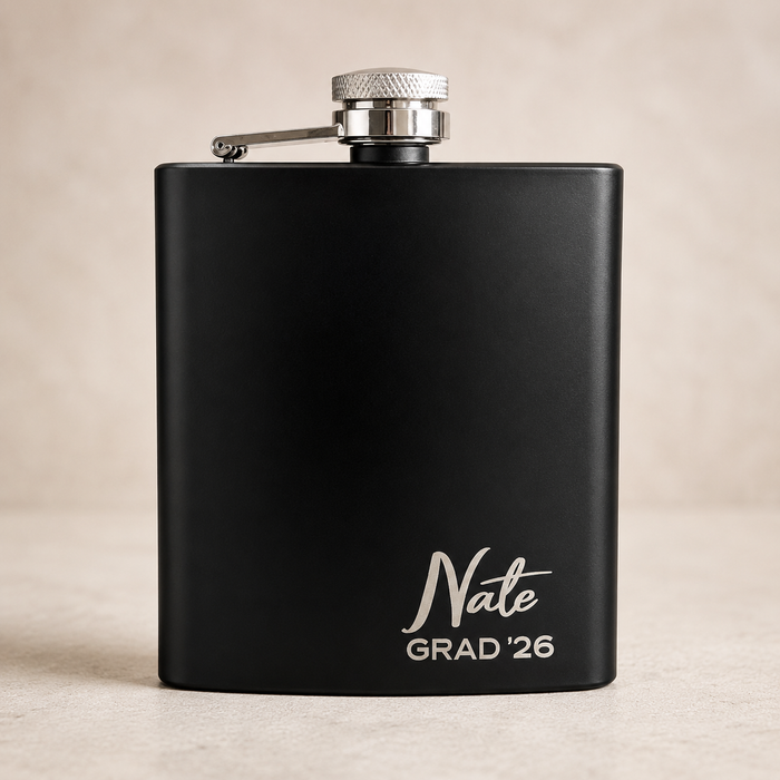 A matte black flask with a silver screw cap and side spout, personalized with the name 'Nate' and 'GRAD '26' in white script and block lettering near the bottom, set against a neutral beige background.